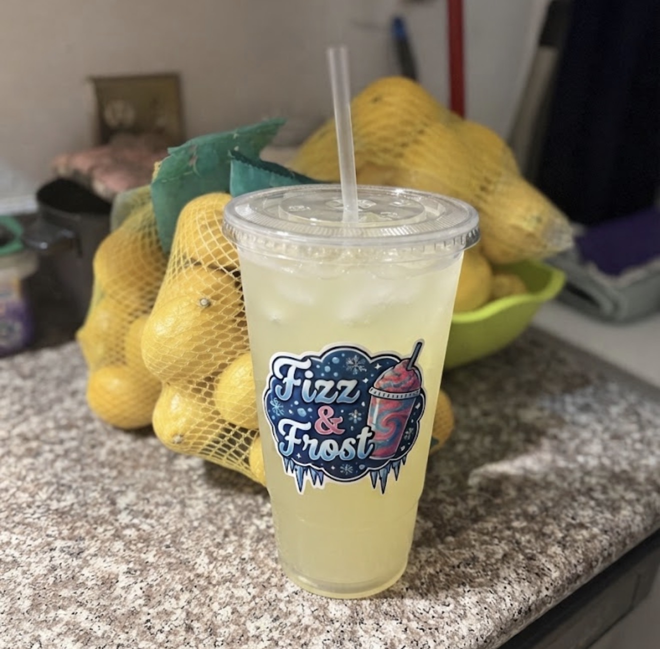 Fresh-squeezed lemonade in a Fizz & Frost cup beside bags of lemons