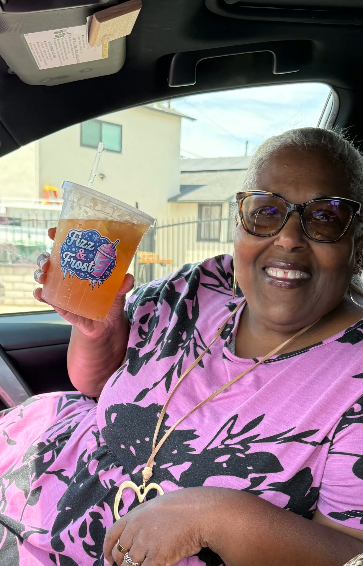 Smiling customer holding up an iced Fizz & Frost drink in her car